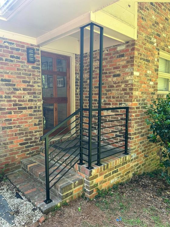 A brick house with a black railing on the porch and stairs.