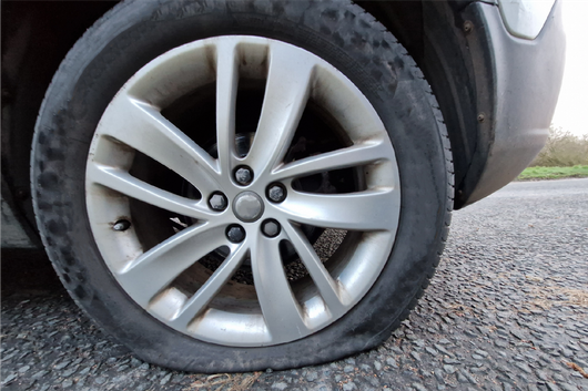 A car with a flat tire on the side of the road.