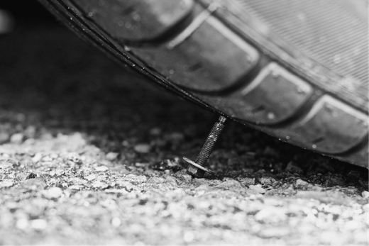 A black and white photo of a tire with a nail sticking out of it.
