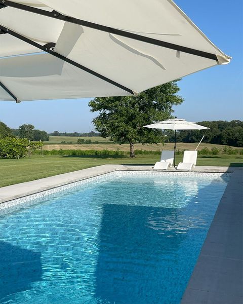 Sunny poolside scene with blue swimming pool, white umbrellas, lounge chairs, and green lawn beyond