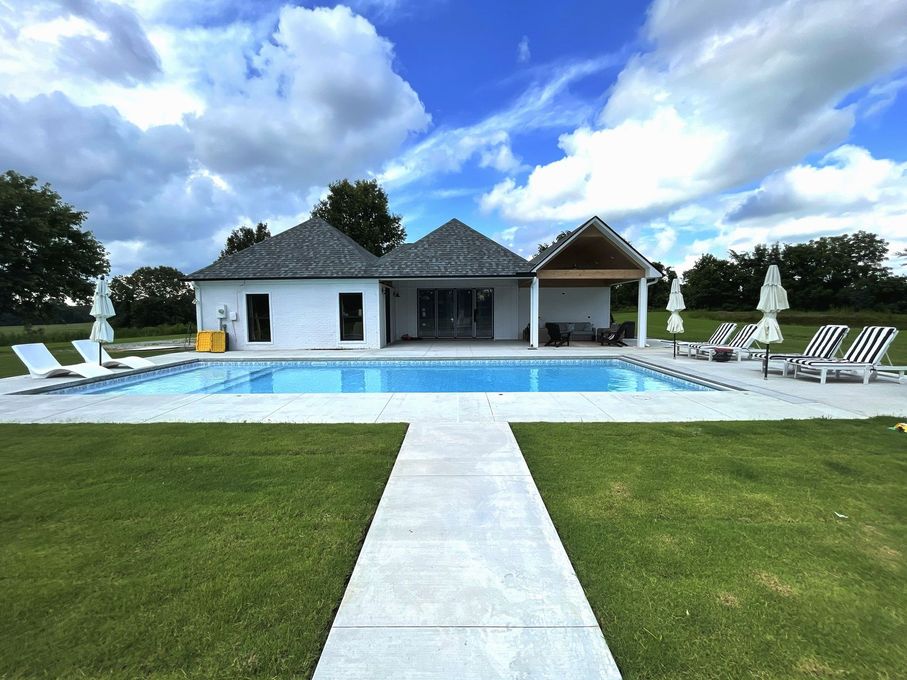 Luxury villa with pool, white lounge chairs, and a green lawn under a partly cloudy sky