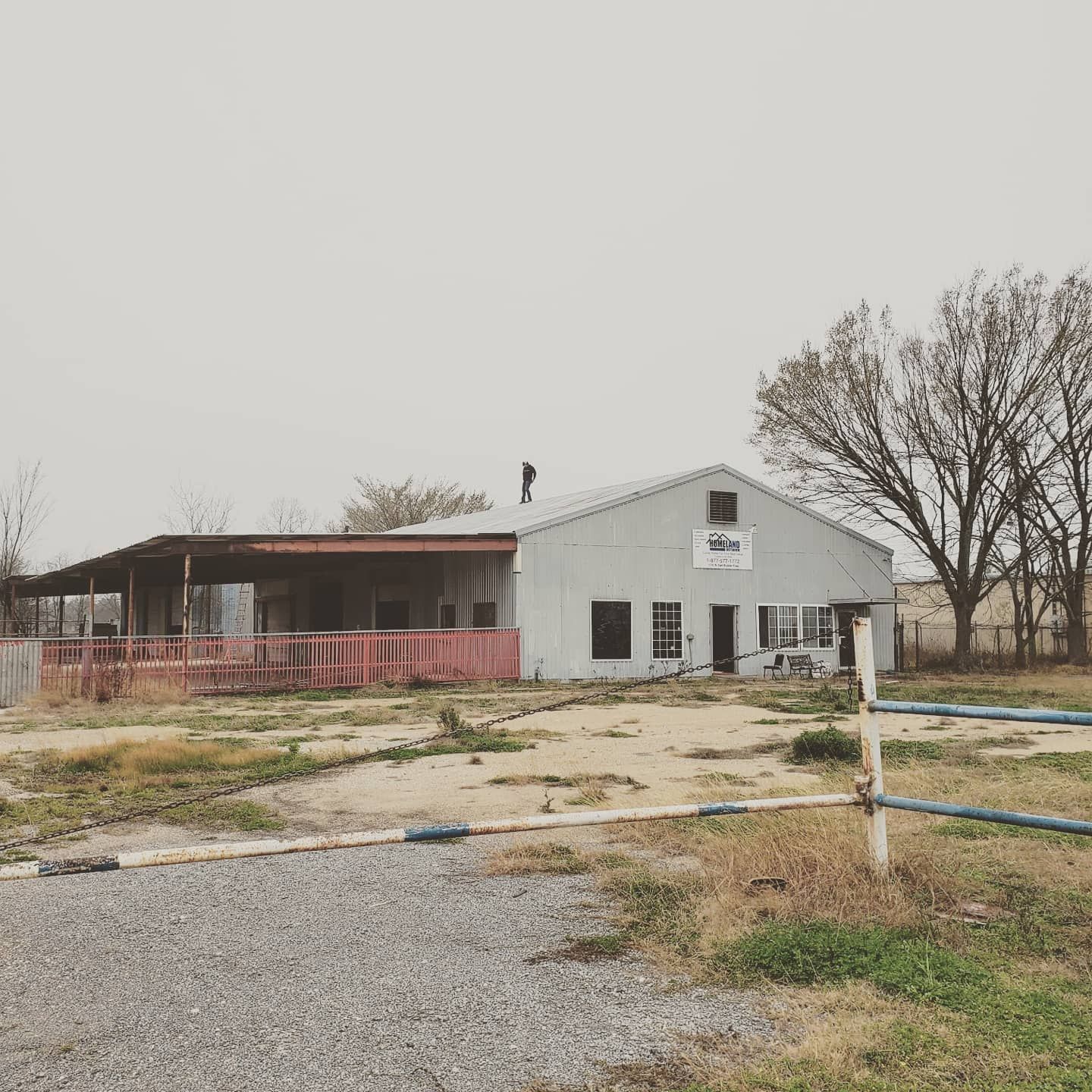 A white house with a red porch is sitting in the middle of a dirt field.
