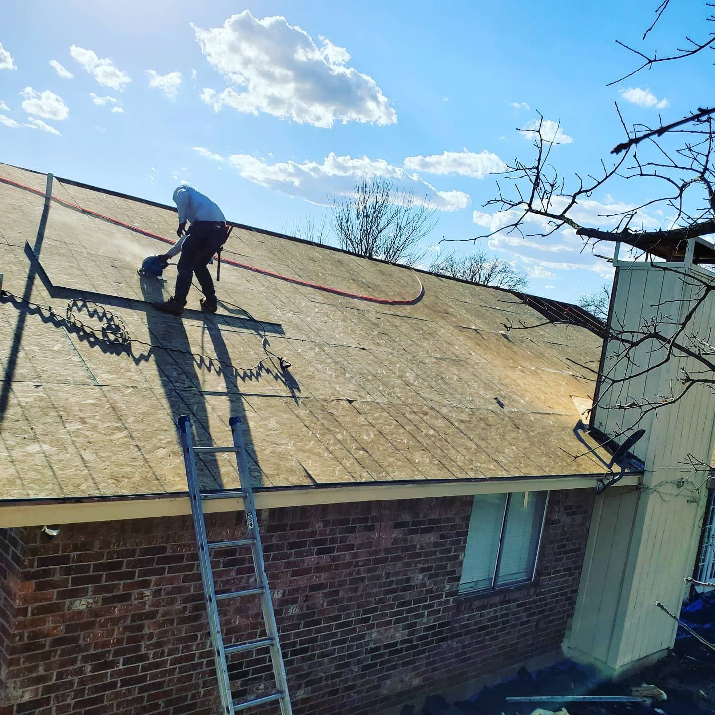 A man is working on the roof of a brick house with a ladder.