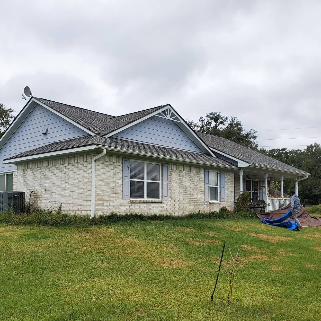 A brick house with a gray roof is sitting on top of a lush green field.