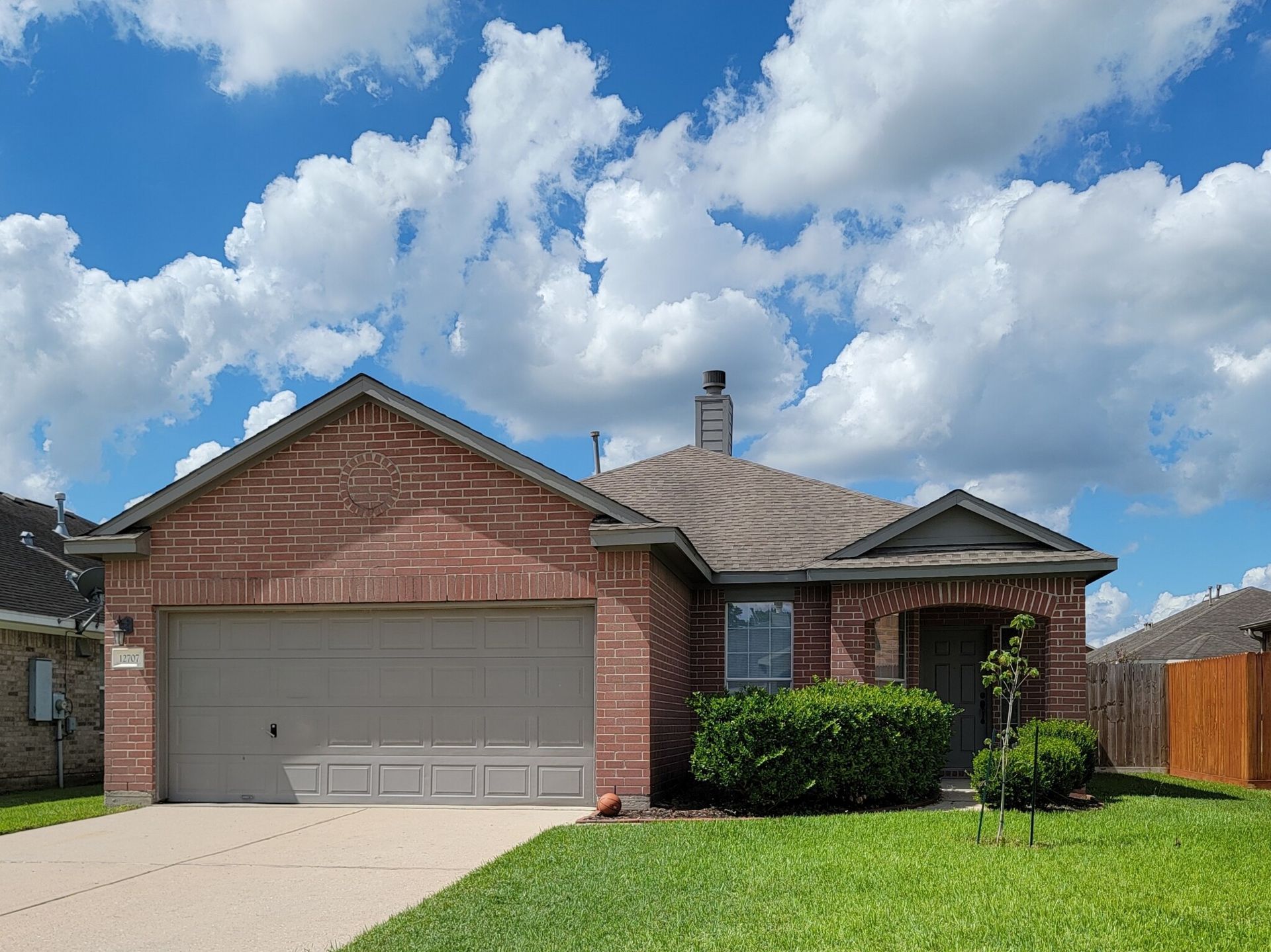 A brick house with a gray garage door and a chimney on the roof.