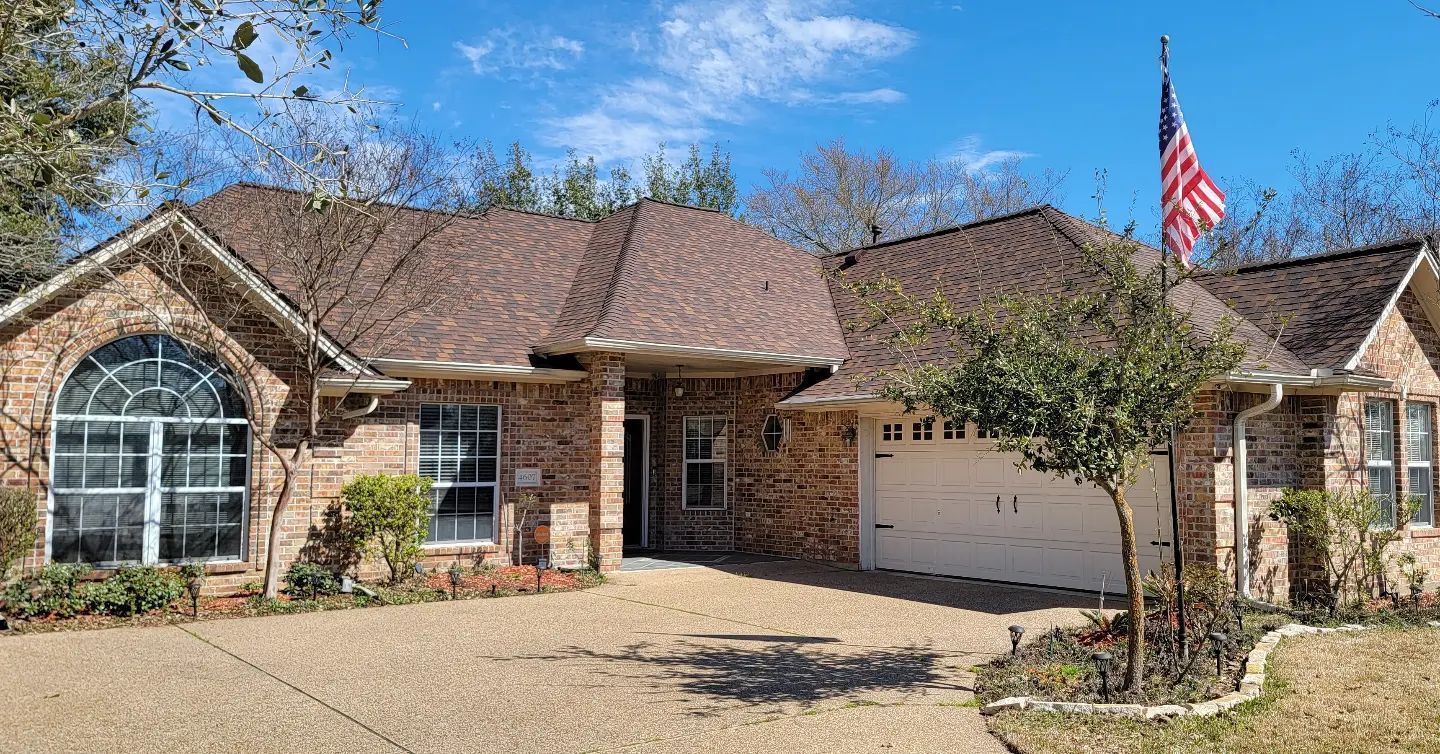 A brick house with a brown roof and an american flag on top of it.