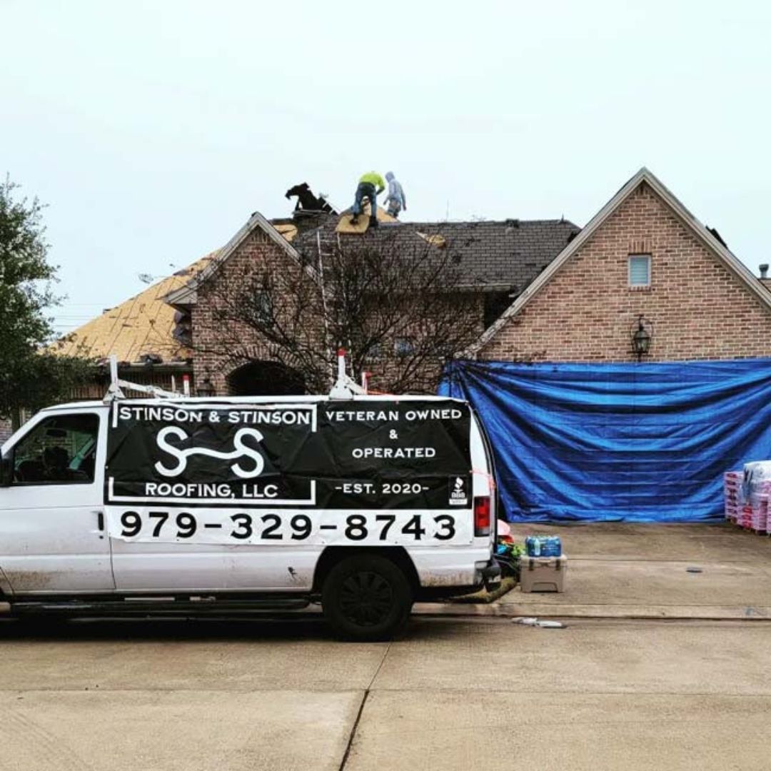 A roofing company van is parked in front of a brick house