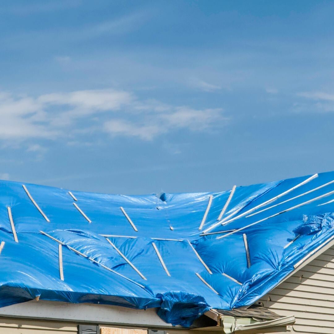 A blue tarp is covering the roof of a house.