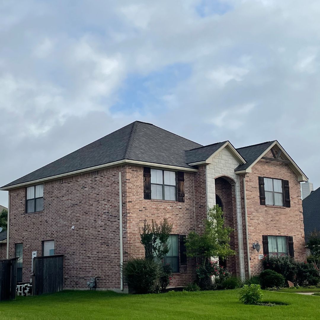 A large brick house with a black roof is sitting on top of a lush green lawn.