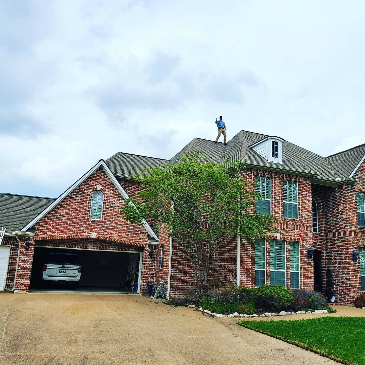 A man is standing on the roof of a large brick house.