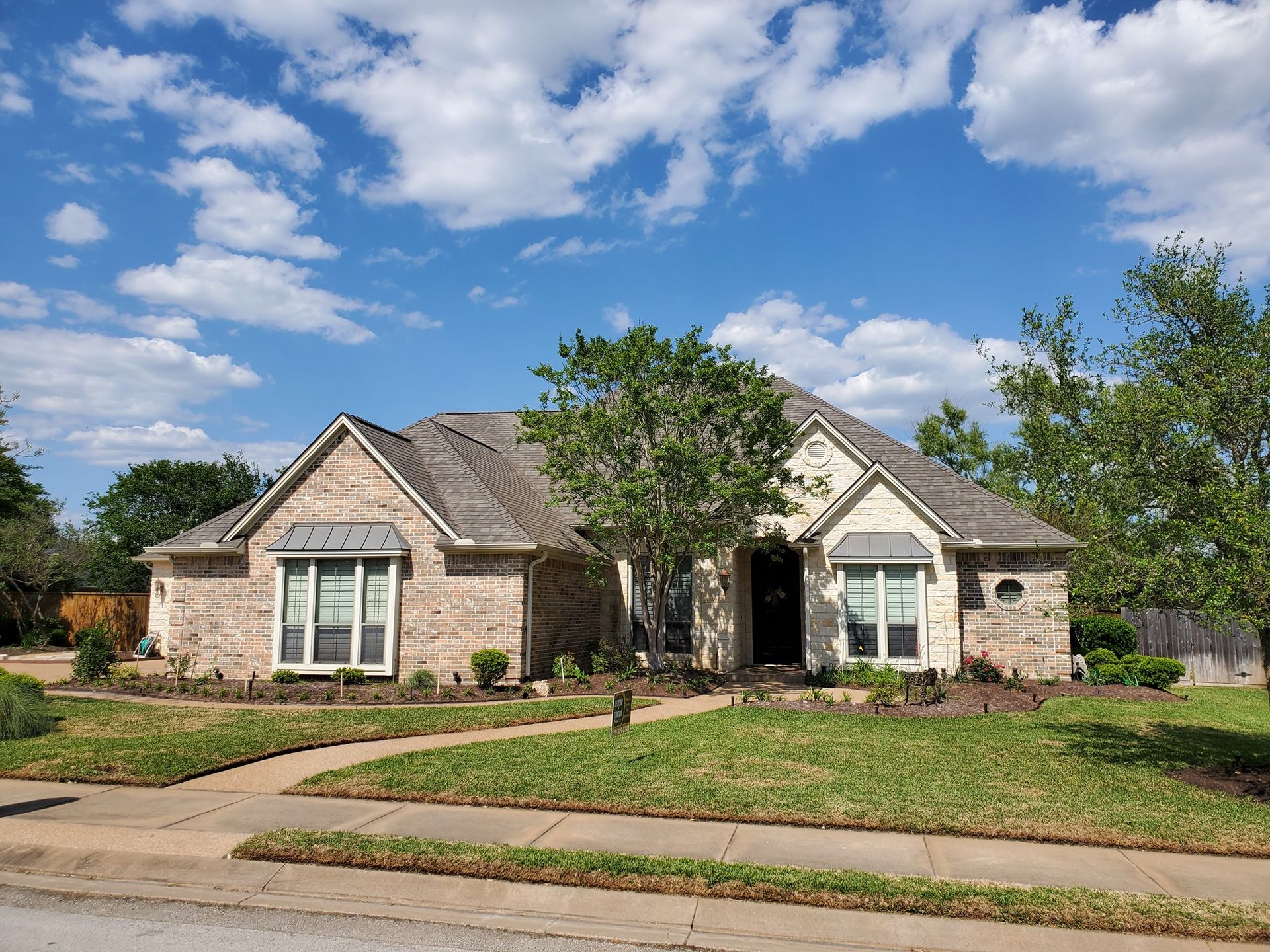 A large brick house with a gray roof is sitting on top of a lush green lawn.
