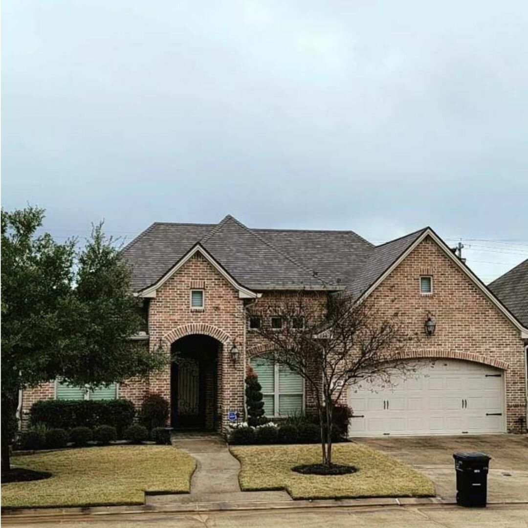 A large brick house with a gray roof and a trash can in front of it.
