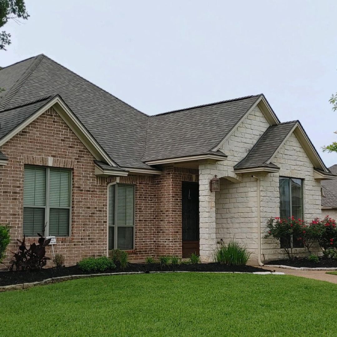 A brick house with a gray roof and a large lawn in front of it.
