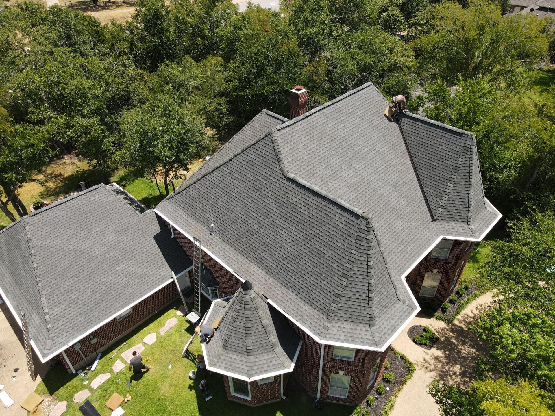 An aerial view of a large brick house with a black roof surrounded by trees.