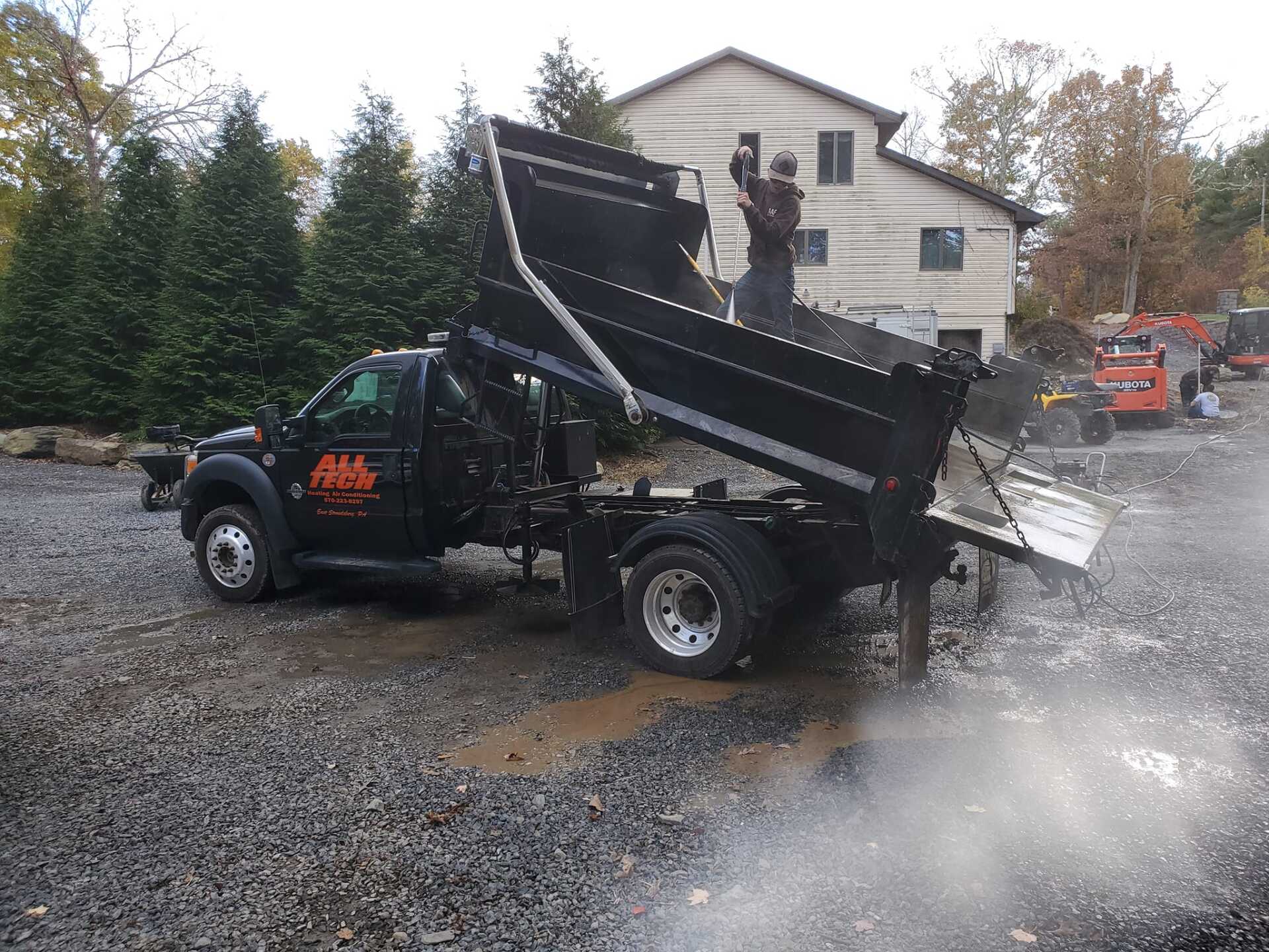 A dump truck is parked in a gravel lot in front of a house.