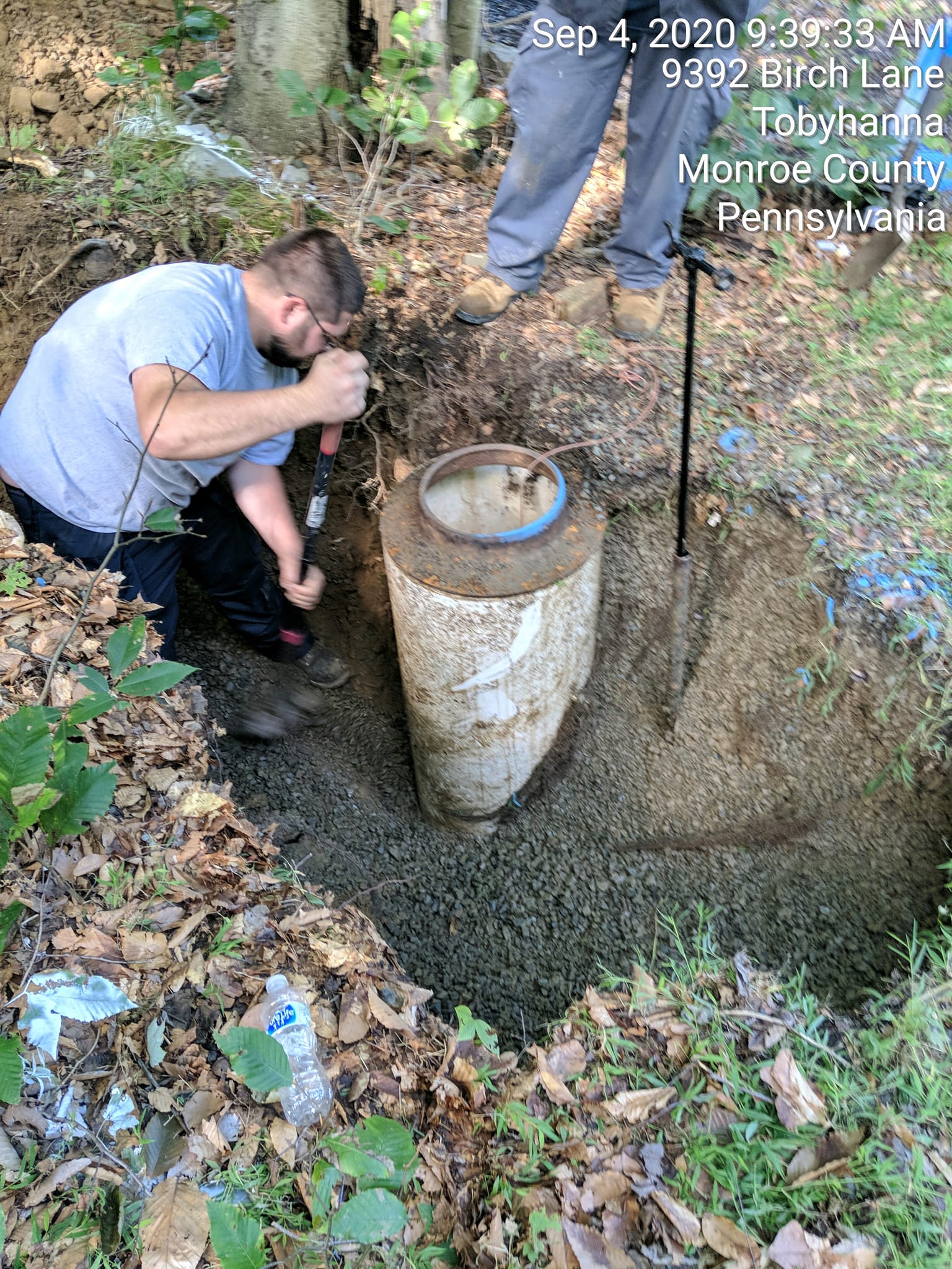 A man is kneeling down in the dirt next to a large pipe.