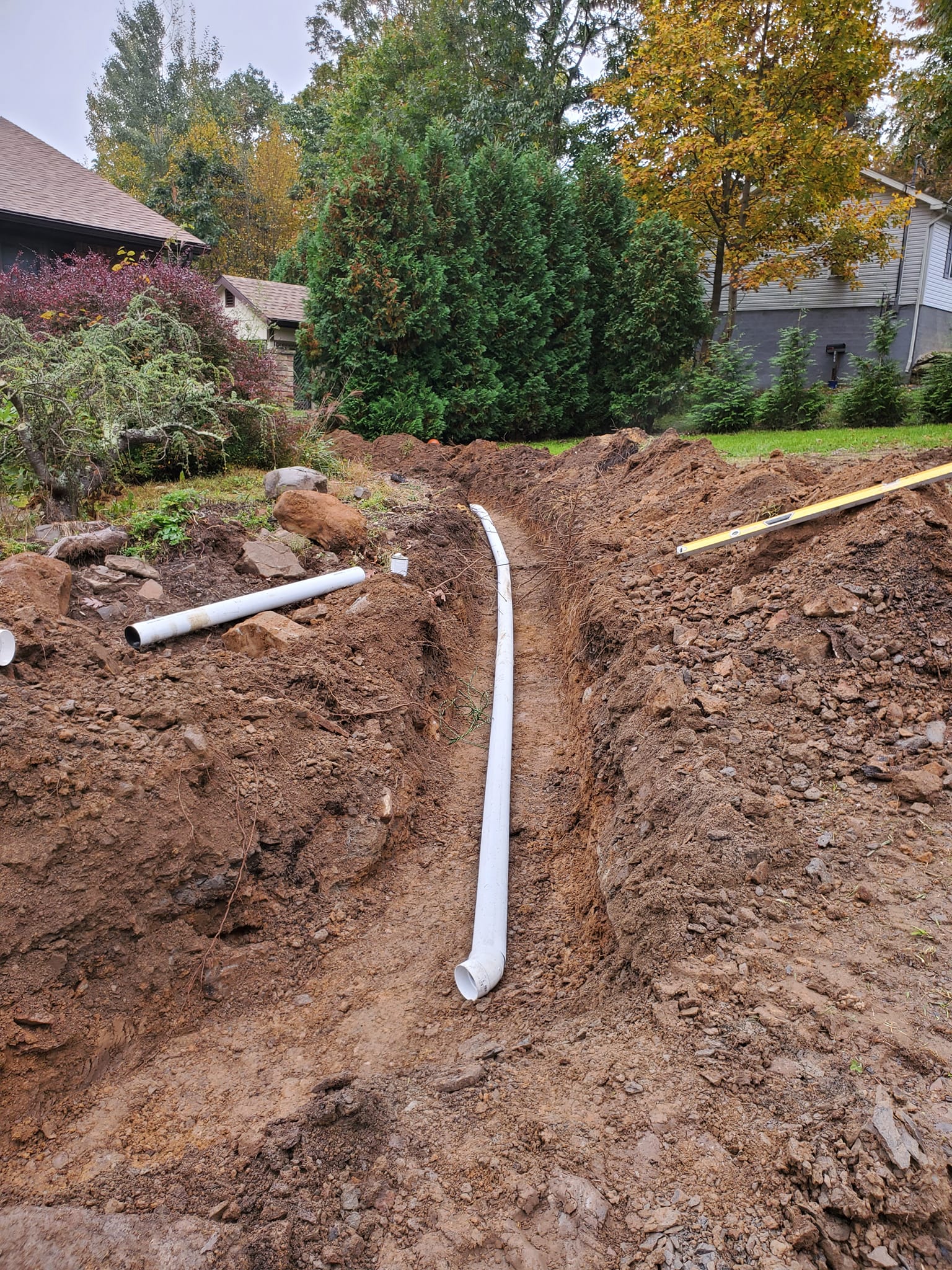 A pipe is being installed in the dirt next to a house.