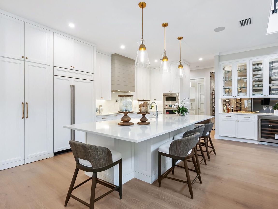 A kitchen with white cabinets , stainless steel appliances , hardwood floors and a large island.