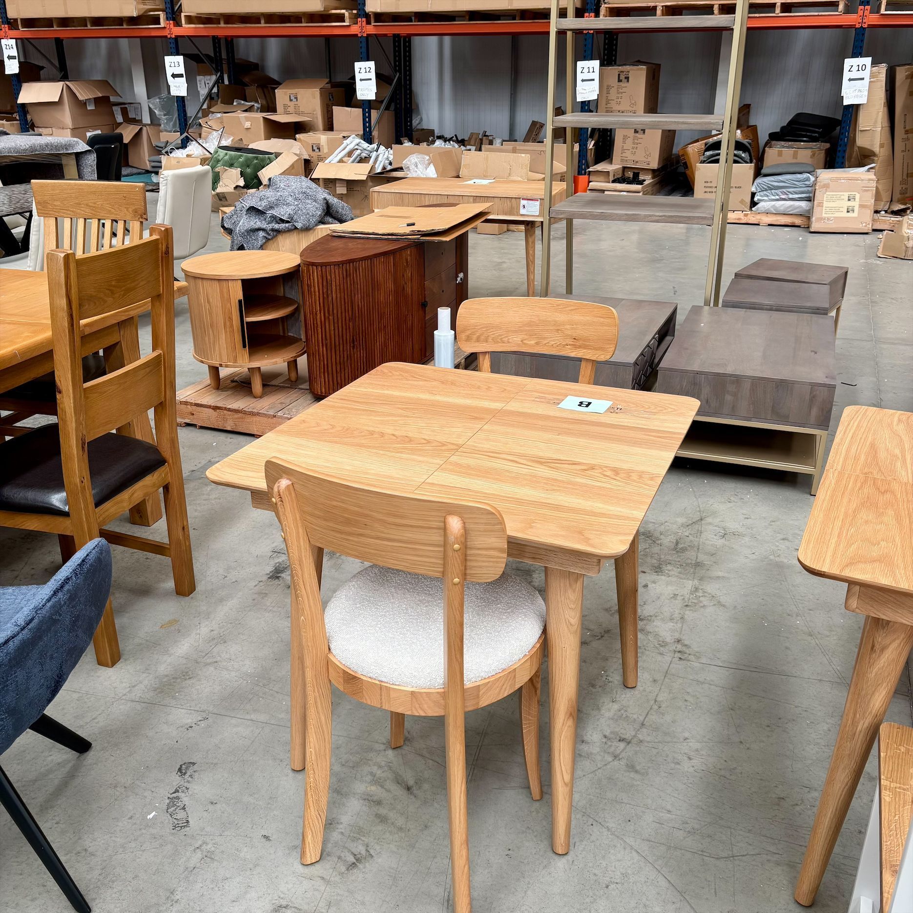 Wooden dining table and chairs in a warehouse showroom with other furniture in the background