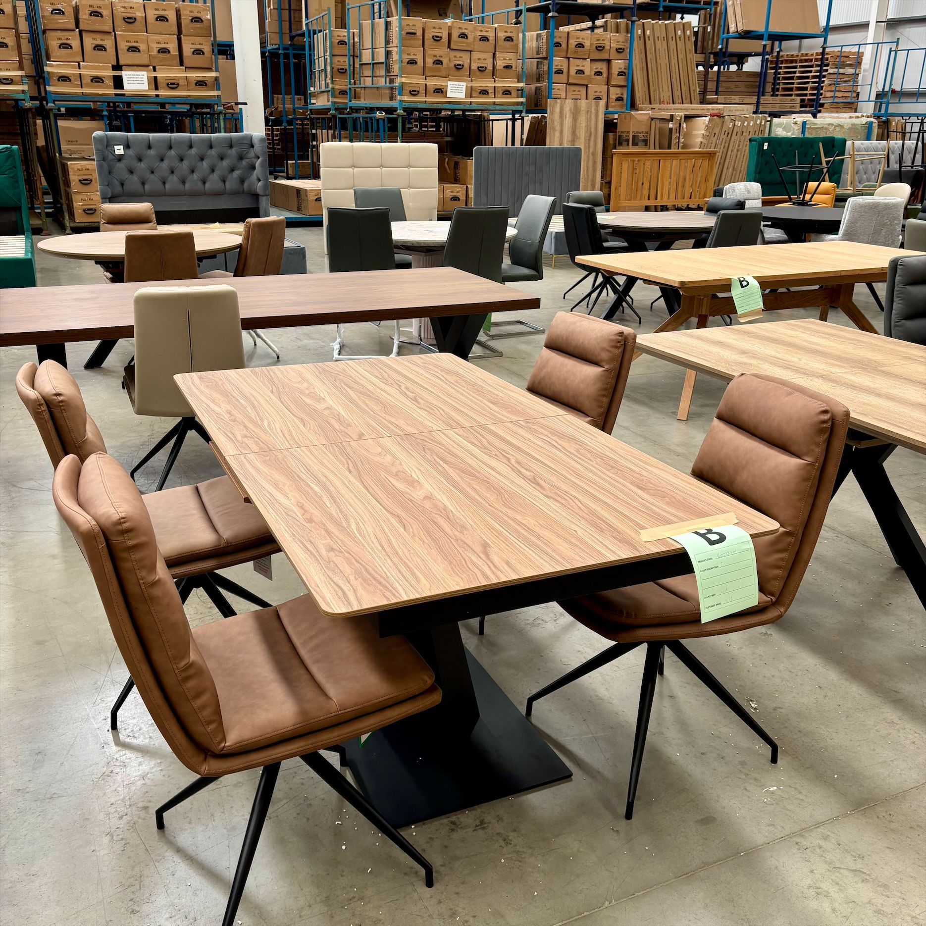Warehouse showroom with wooden tables and padded brown chairs on a concrete floor
