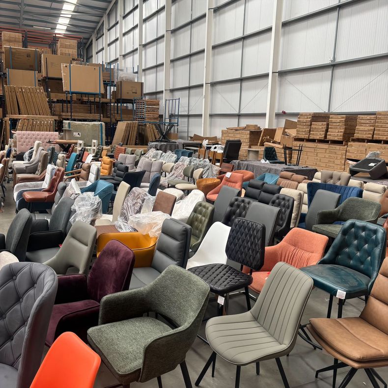 Warehouse filled with rows of colorful upholstered chairs and stacked boxes in the background