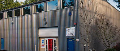 A corrugated metal building with a red door and small windows. A sign hangs on the wall.