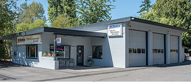 Auto repair shop with three garage doors; gray building with trees in the background.