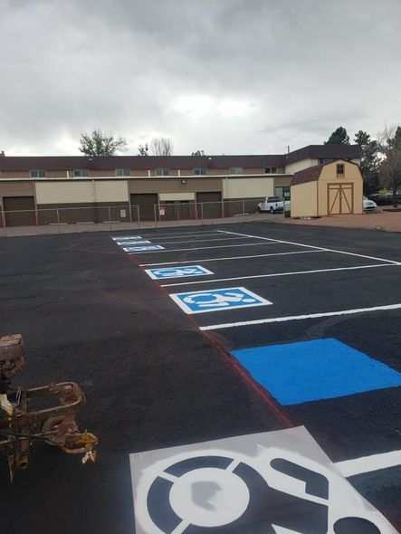 Newly painted accessible parking spaces in a lot. Blue and white wheelchair symbols on black asphalt.