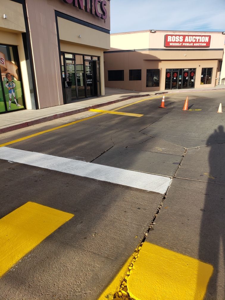 Parking lot with painted yellow and white markings; stores and orange traffic cones in background.