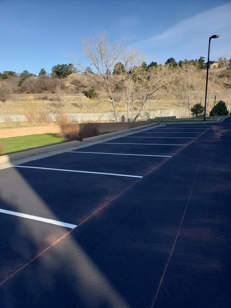 Empty outdoor parking lot with white painted lines and a hill in the background under a blue sky.