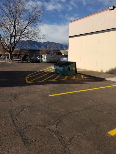 Exterior shot of parking area with dumpsters, a building, and mountains in the background under a blue sky.