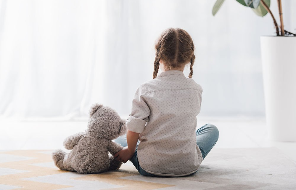 A little girl is sitting on the floor holding a teddy bear.