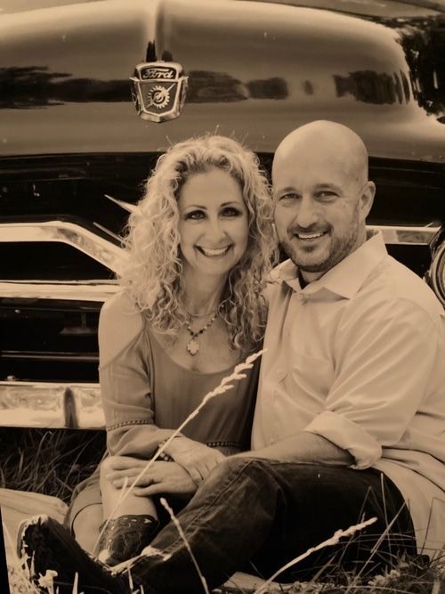 A man and a woman are posing for a picture in front of an old car