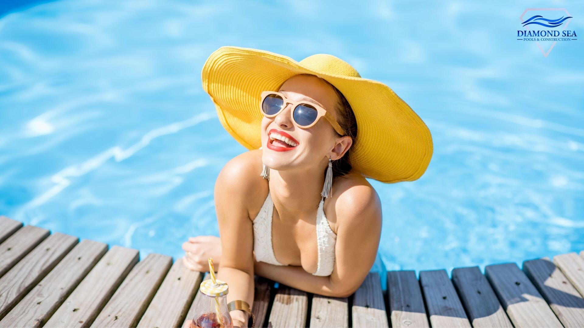 a woman wearing a white bikini and yellow sunhat leaning against the edge of an Austin swimming pool and smiling with a drink in her hand