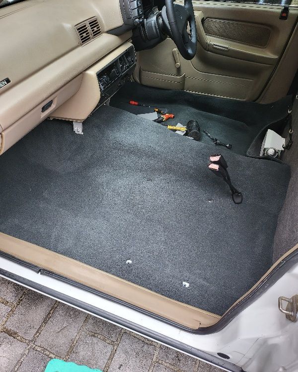 Gray car interior with new carpet installed, beige trim, tools visible.
