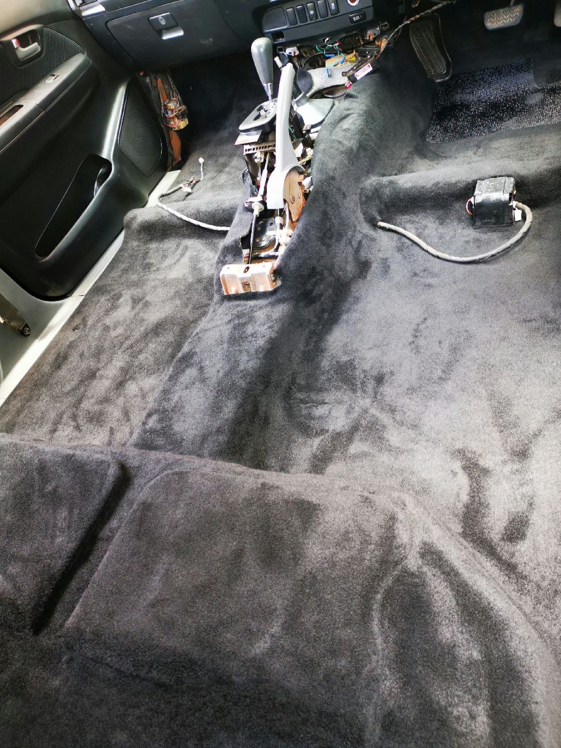 Dark gray car interior with the carpet installed, revealing the gear shift and other mechanics.