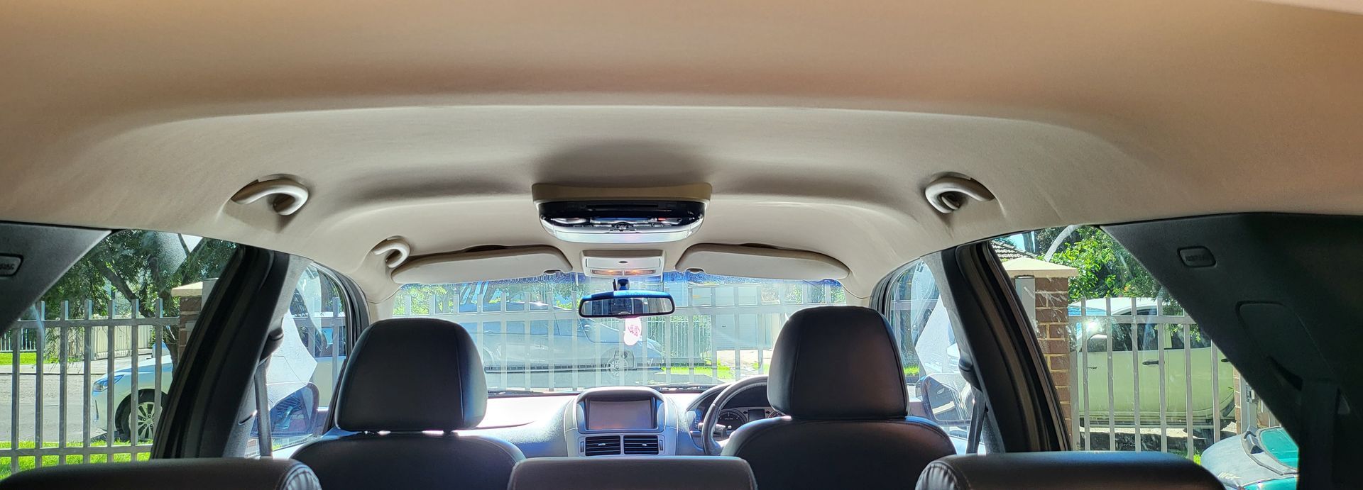 Interior view of a car's roof, showing overhead console, seats, and windows with outdoor view.