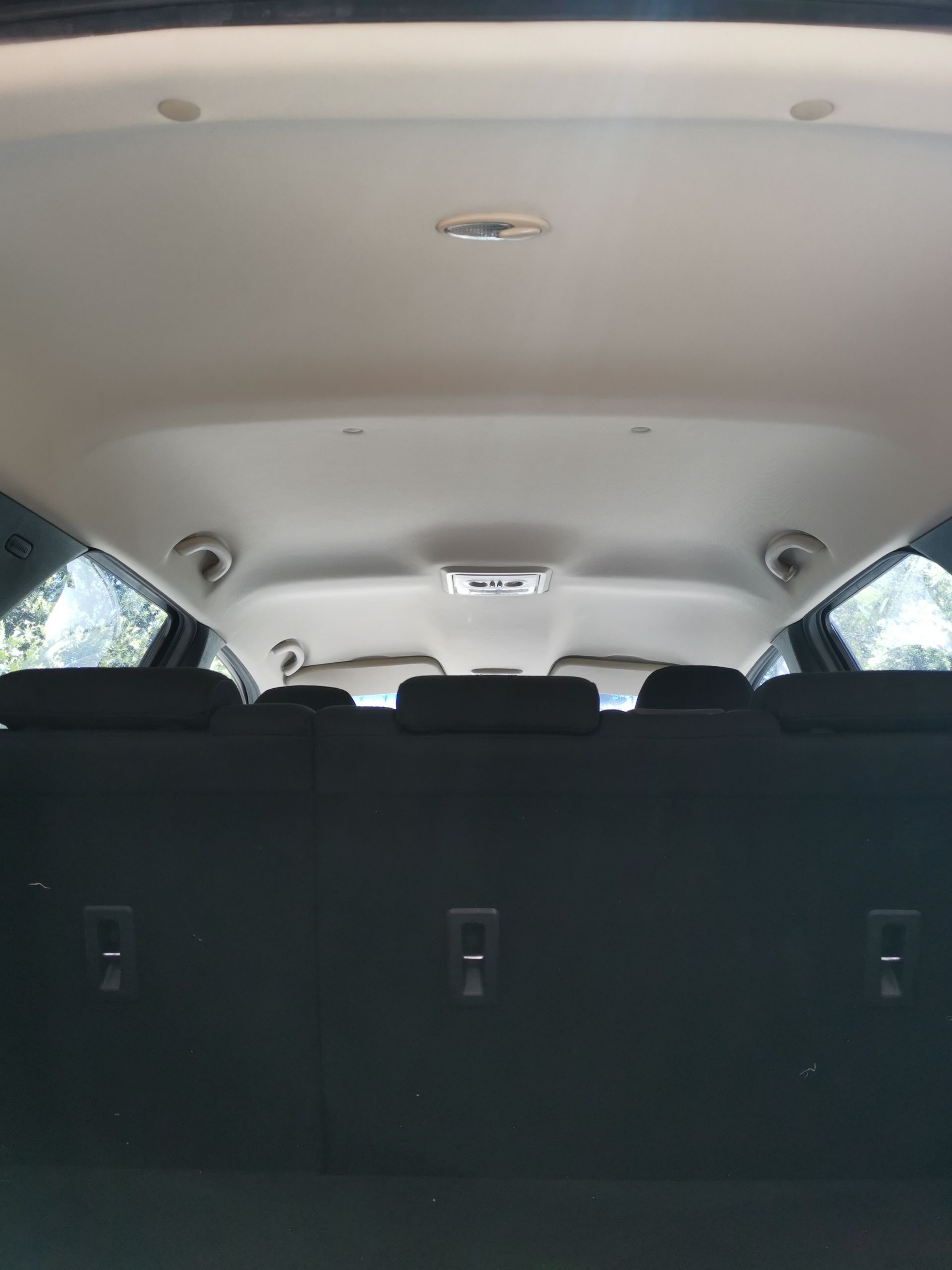 Interior view of a car trunk with black seats and a beige ceiling, showing rear seats and lights.
