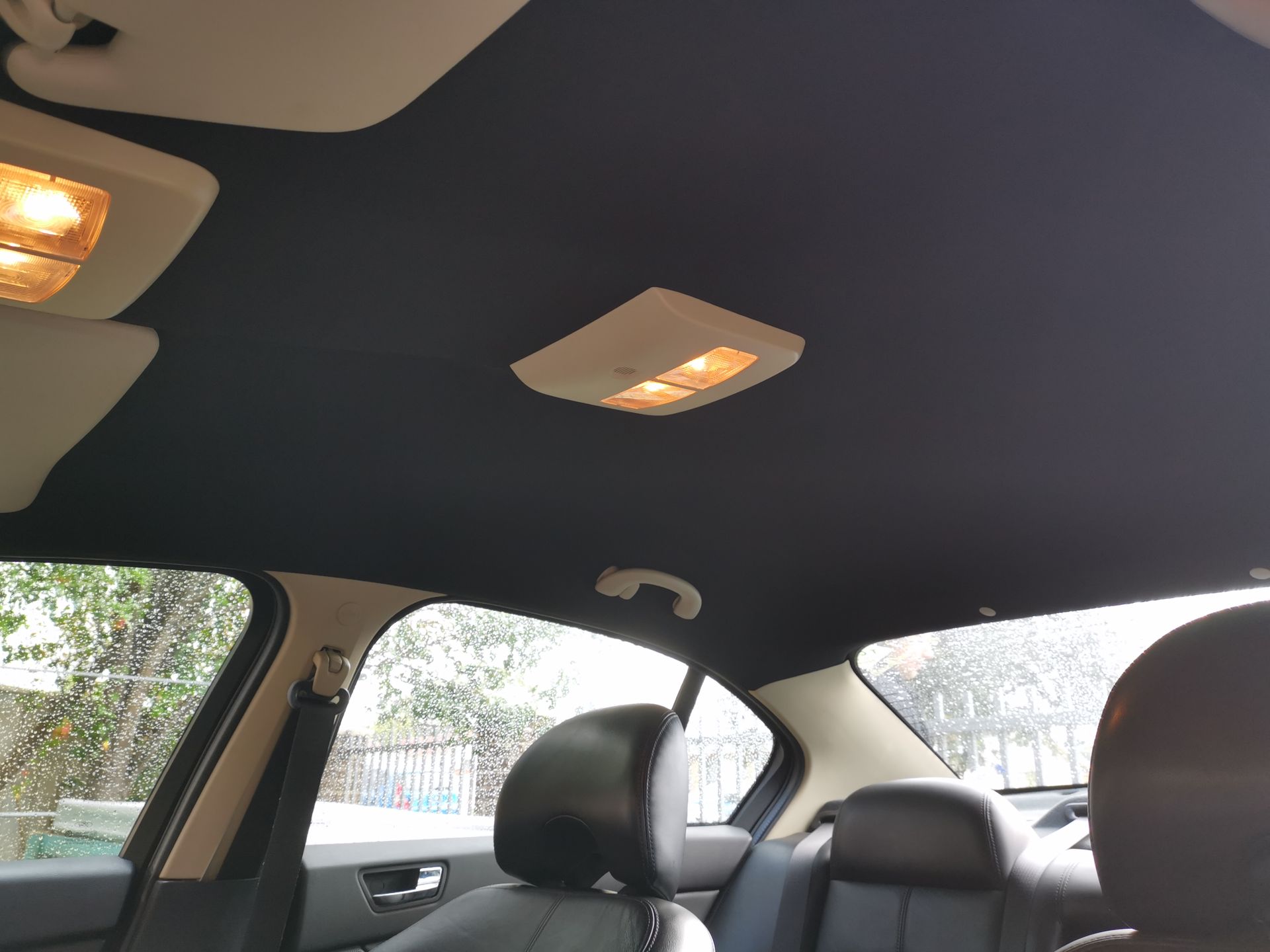 Black car interior ceiling with lights and seats visible.