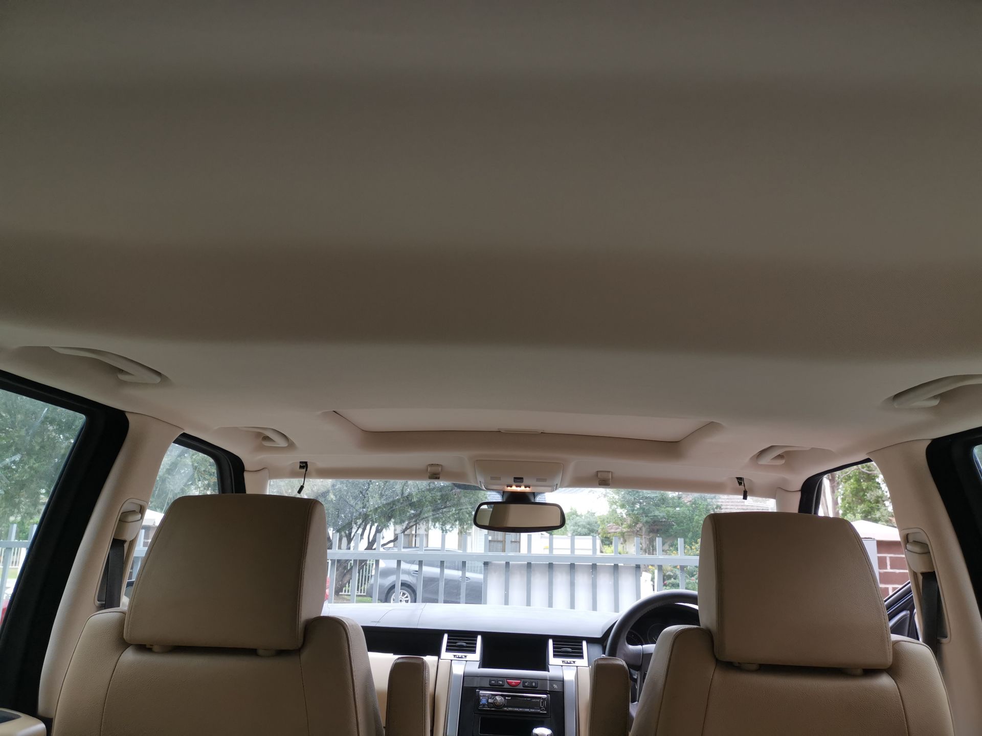 Interior view of a beige car cabin with two front seats, steering wheel, and a sunroof.