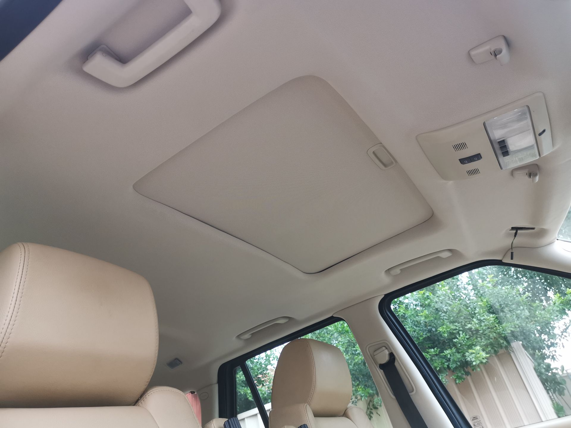 Tan car interior with closed sunroof, tan leather seats, and window visible.