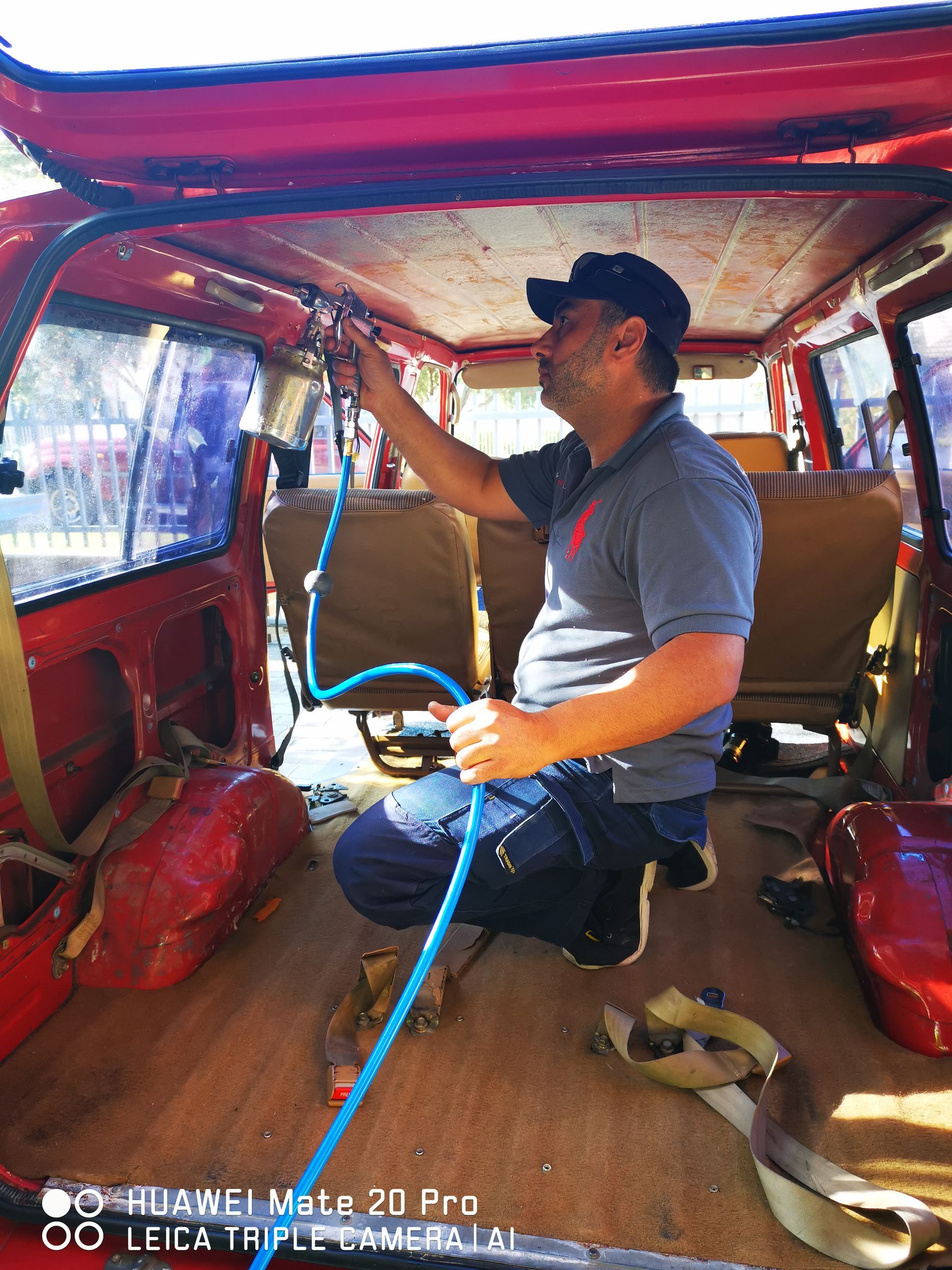 Man inspecting inside a red vehicle. He's holding a blue hose, and the interior is mostly disassembled.