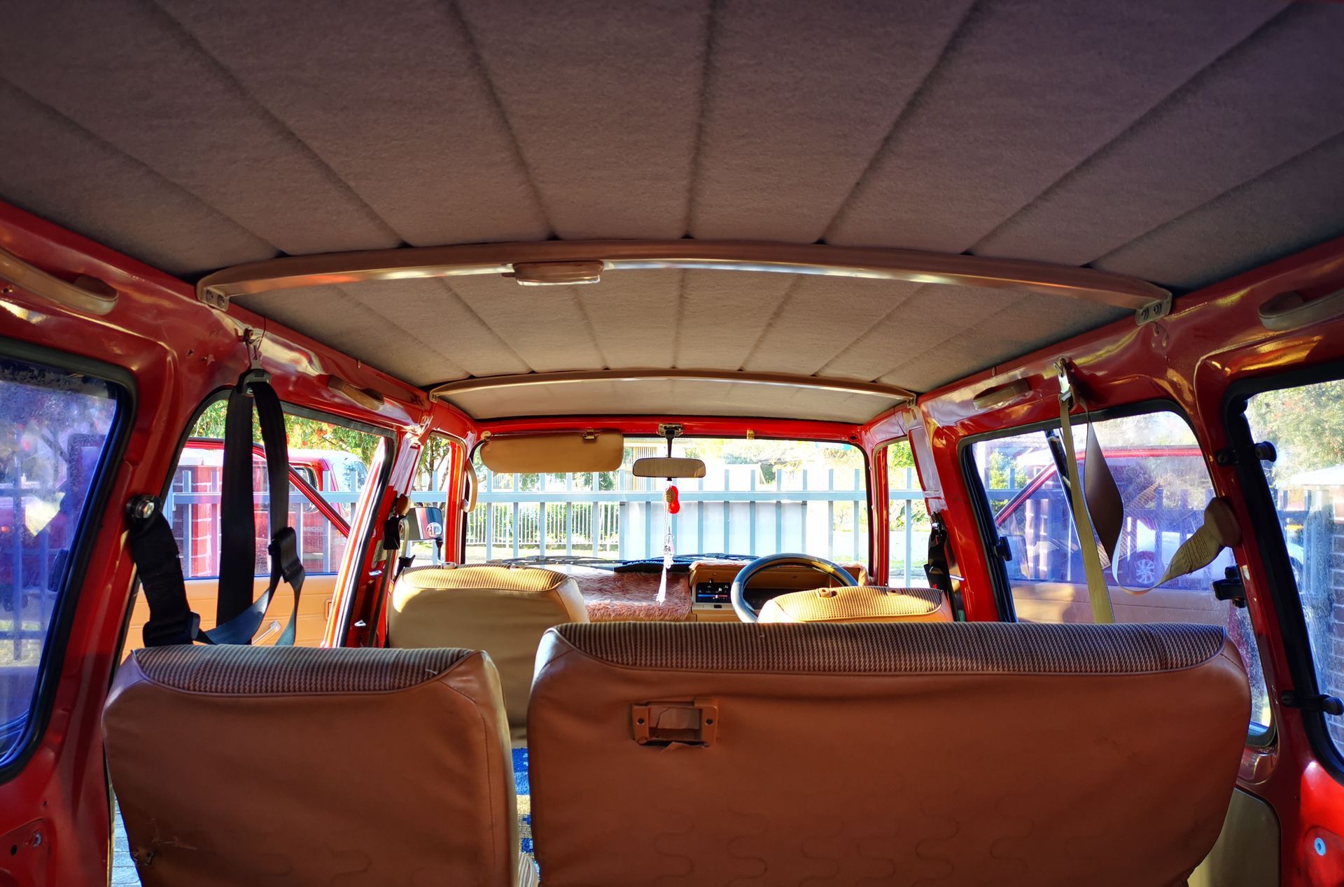 Interior of a red car, showing the roof, seats, and windows. Beige and red color scheme.