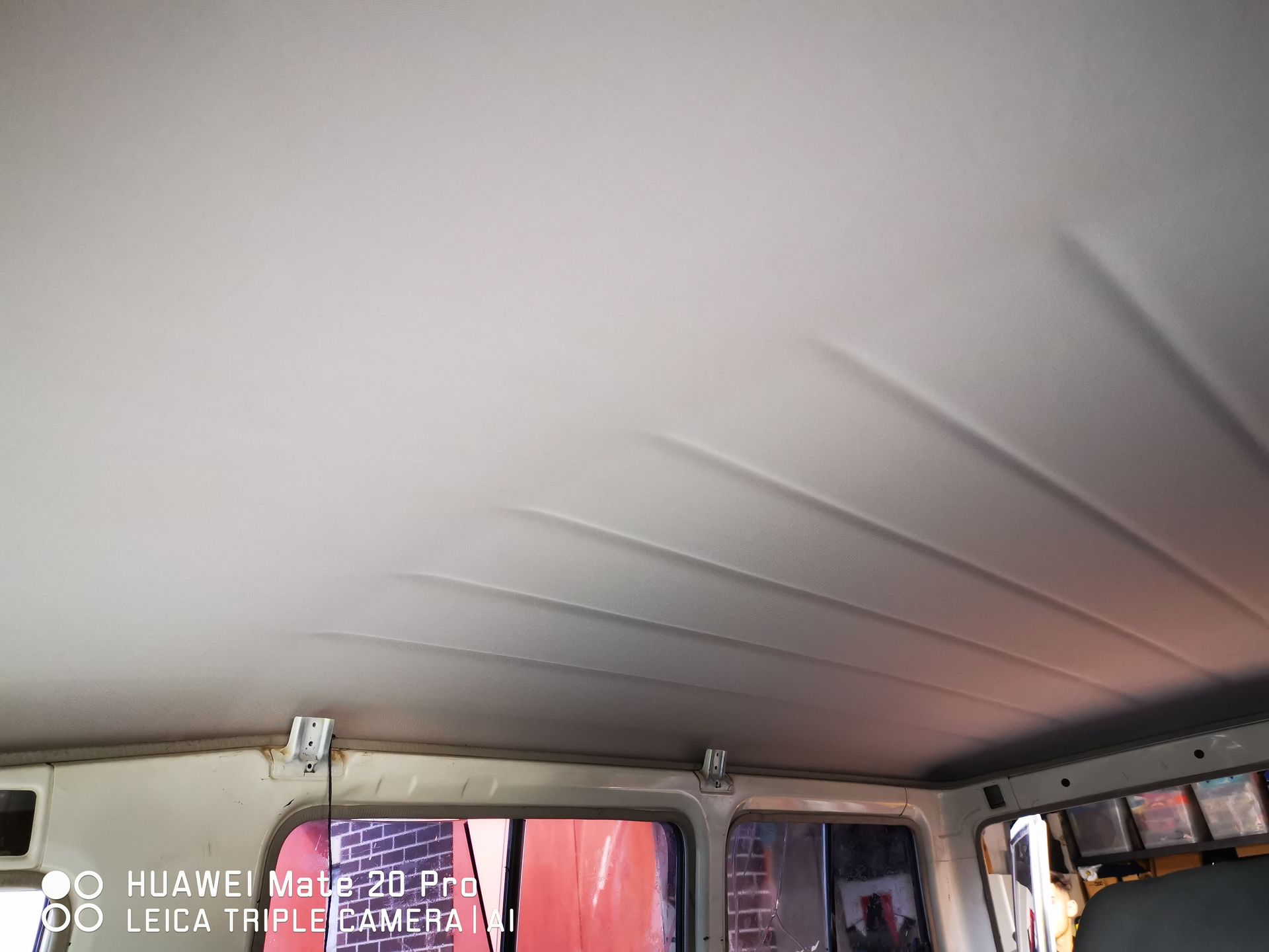 Interior of a vehicle's ceiling with sagging, light-colored fabric. Windows and support beams are visible.