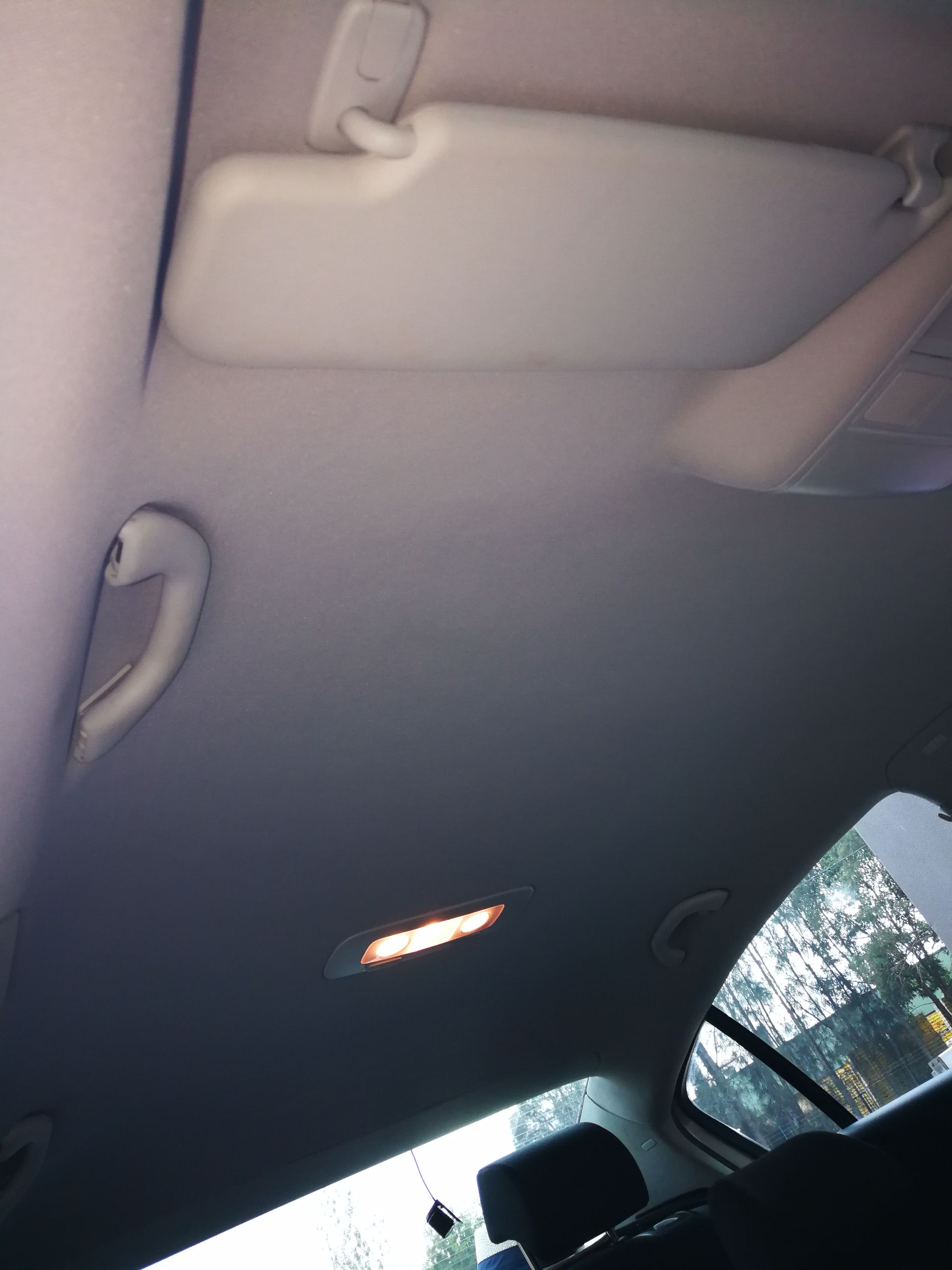 Car interior, looking up: beige headliner, sun visor, handle, and light fixture.