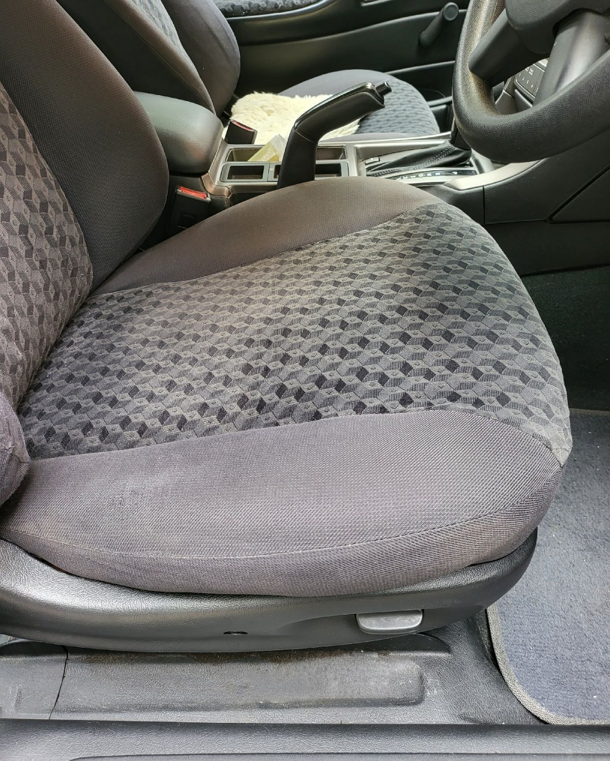 Gray fabric car seat with patterned center section. Armrest and steering wheel visible in the background.