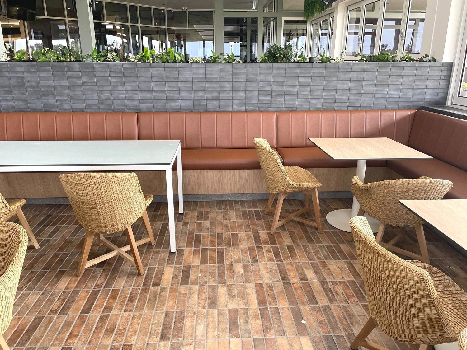 Outdoor restaurant seating: brown wicker chairs, brown and white tables, brown tiled floor, and a brown bench.