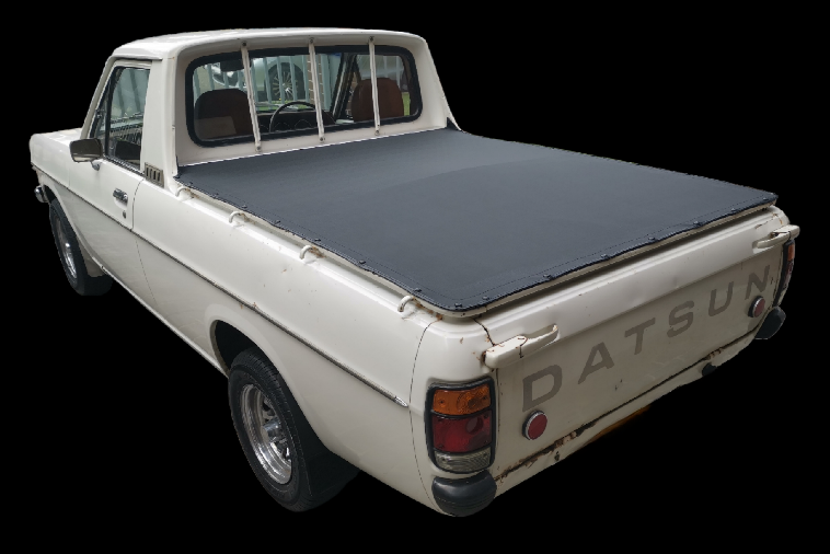 White Datsun pickup truck with a black tonneau cover, on a black background.