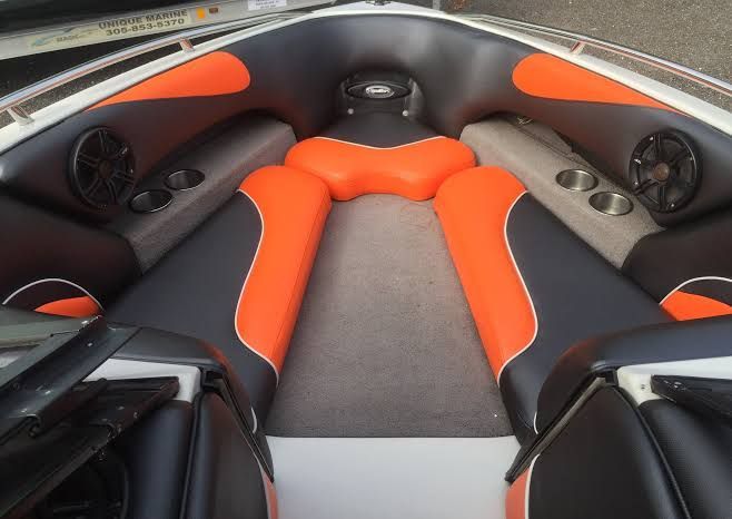 Interior of a boat with black, orange, and gray seats, speakers, and cup holders.
