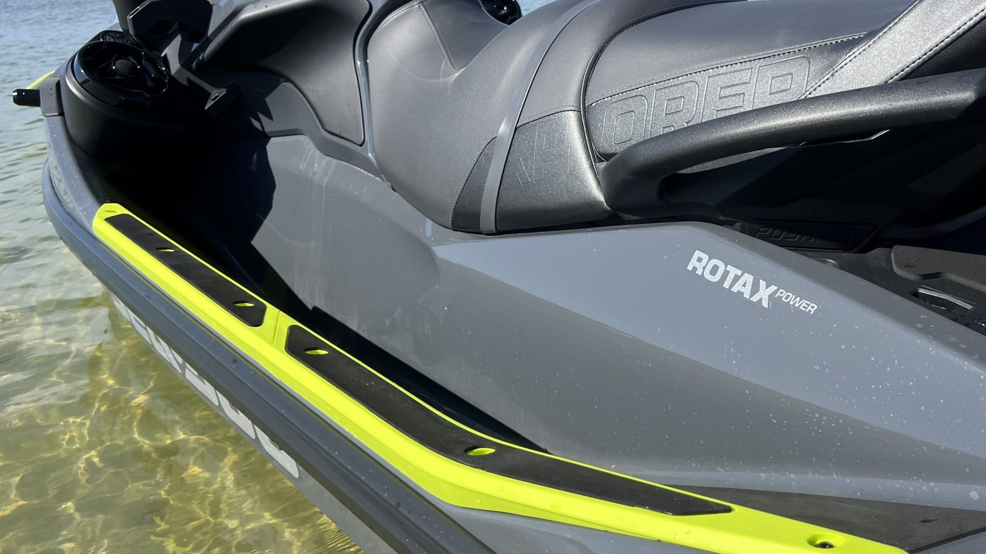 Jet ski, gray body with neon yellow accents, Rotax engine logo, next to water.